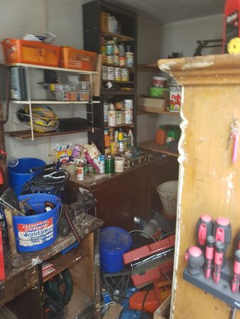 Unordentliche Werkstatt mit Werkzeugen, Regalen, Schraubenziehern und Farbeimern.