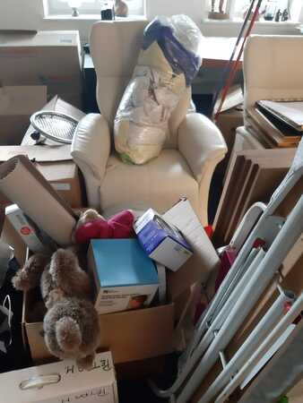 Voller Umzugskarton, Kartons und Verpackungen stapeln sich auf Sessel in chaotischem Raum.