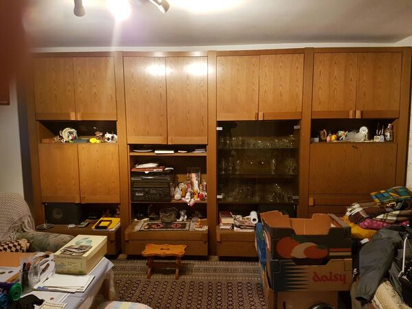 Großer Wohnzimmerschrank aus Holz mit Glasvitrine, vollgestellt mit Deko und Umzugskartons.